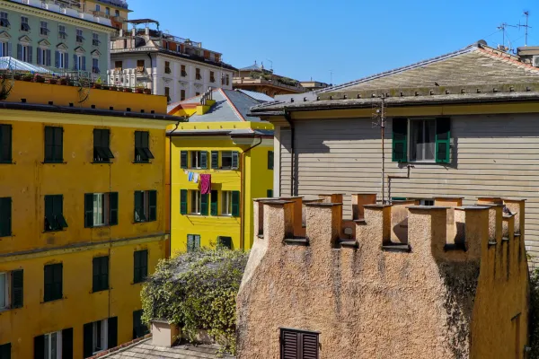 Fachadas de edificios amarillos con persianas verdes y mampostería en Génova bajo un sol brillante.
