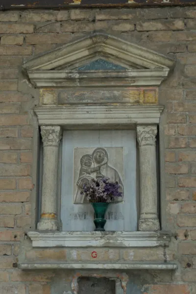 Religious sculpture of the Madonna and Child with flowers in a stone niche, suitable for wall decor.
