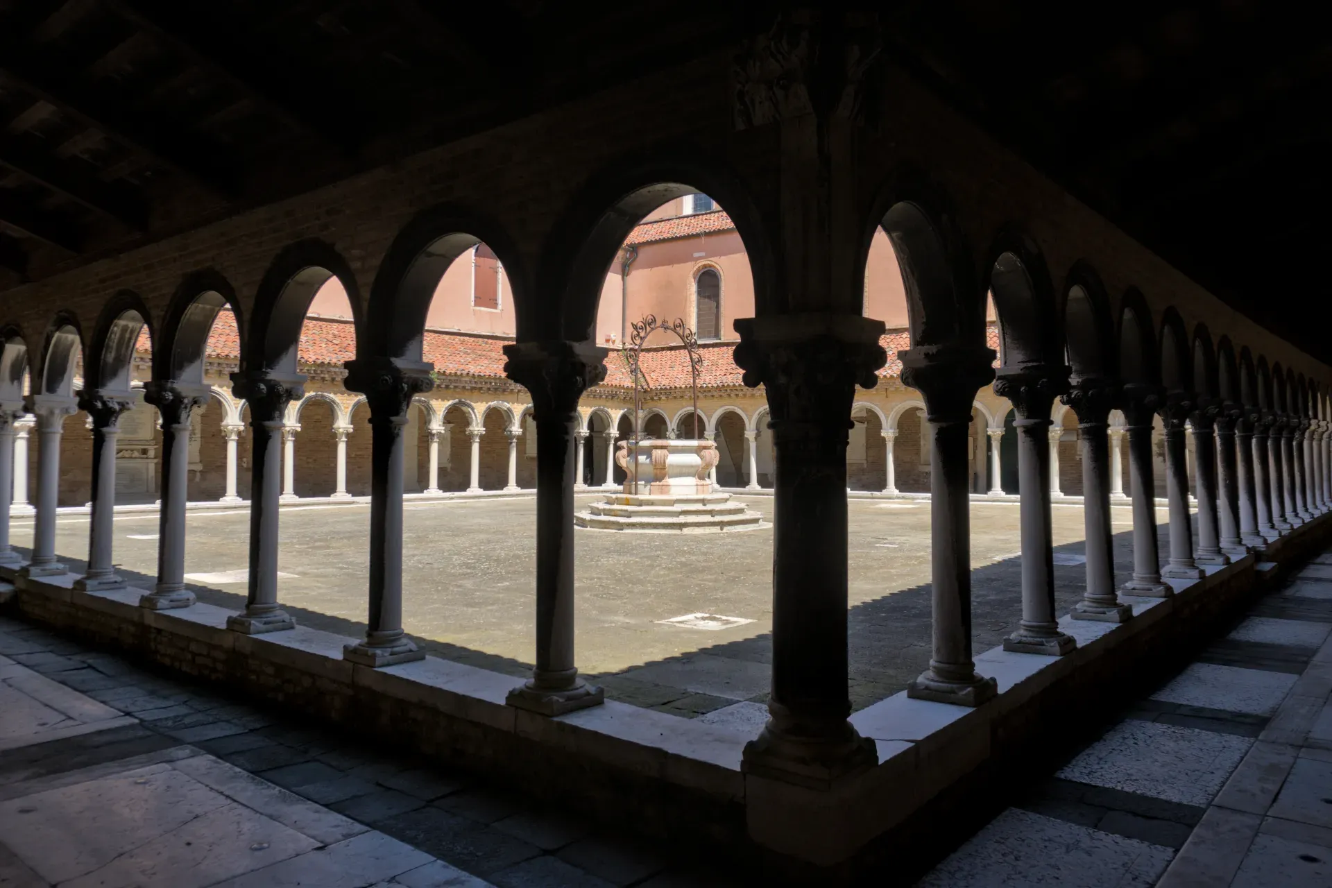 Cour architecturale au cimetière San Michele à Venise avec arches, colonnes et un puits.