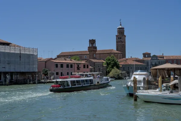 Circulation de bateaux sur le canal de l'île de Murano, Venise, avec des bâtiments d'église historiques à l'arrière-plan sous le soleil.