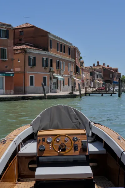 Blick von einem Boot auf die Kanäle von Murano, Venedig, mit traditionellen Gebäuden und klarem Himmel.