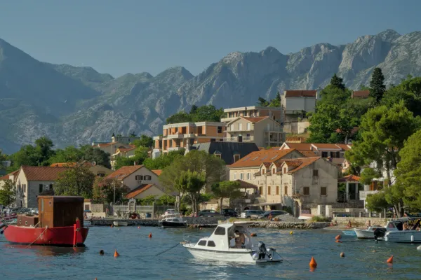 Vista pintoresca de la Bahía de Kotor con encantadoras casas, barcos y majestuosas montañas al fondo, que representan una escena de bondad.
