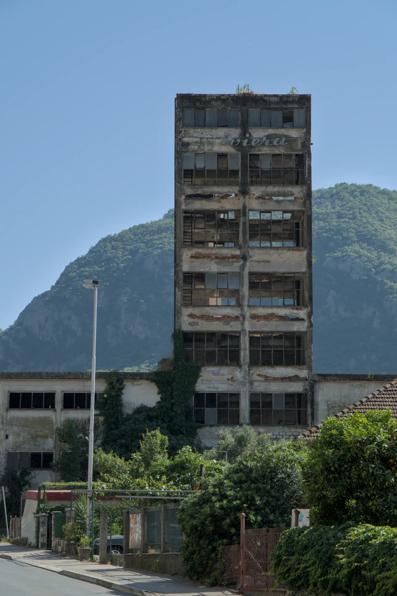 Stara višespratna zgrada u Kotoru, Crna Gora, sa prozorima i planinskim pejzažem u pozadini.