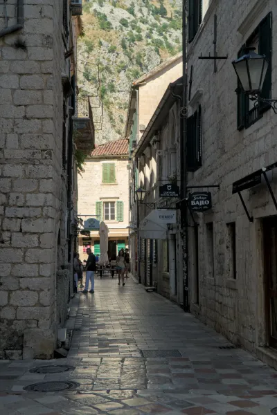 Sunlit street in the old town of Kotor, Montenegro, with stone buildings and mountain view.