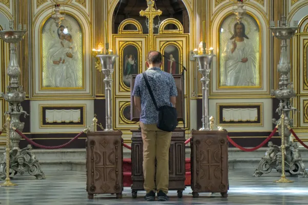 Un hombre se para reverentemente ante un iconostasis ortodoxo, adornado con patrones dorados e iconos.