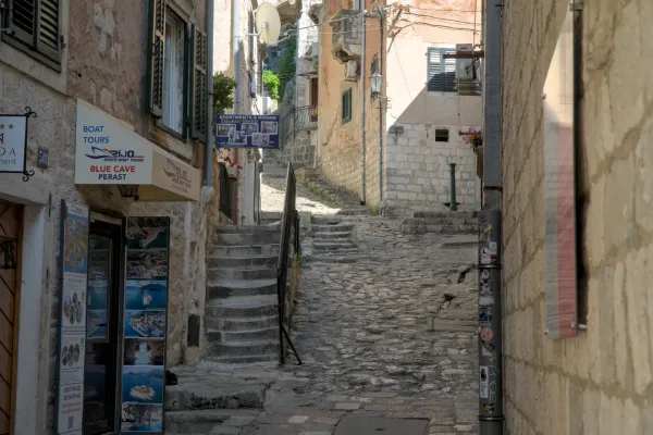 Steep cobblestone alley in Kotor, Montenegro, with stone buildings and a stone staircase leading upwards.