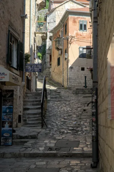 Steep cobblestone alley in Kotor, Montenegro, with historic buildings and stone steps, featuring dramatic lighting.