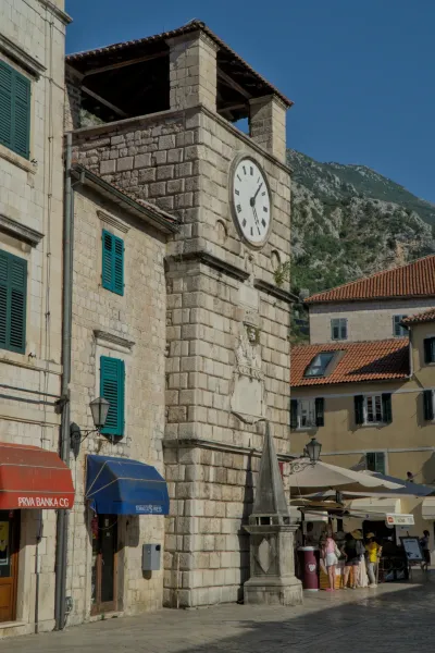 Stone clock tower in Kotor, Montenegro, with green shutters and a mountain in the background.