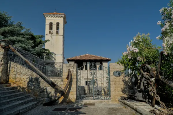 Una vieja ancla oxidada yace frente a una escalera de piedra, junto a un esbelto campanario.
