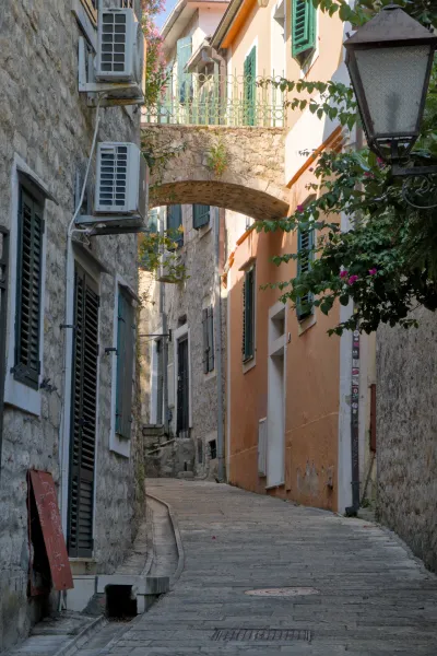 Una estrecha calle de piedra en Herceg Novi bajo un arco de piedra con edificios de tonos cálidos.