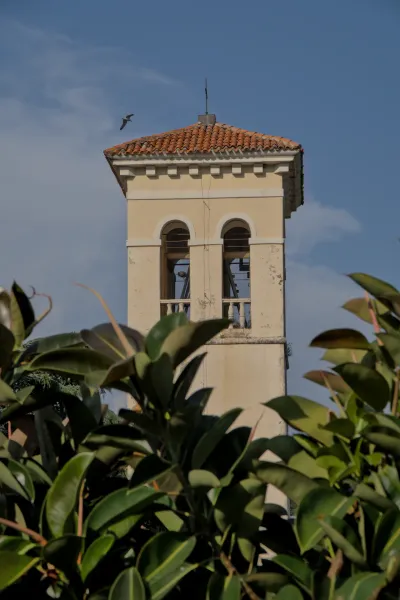 Venecijanski zvonik se uzdiže iznad bujnog zelenog lišća, ptica leti na plavom nebu.