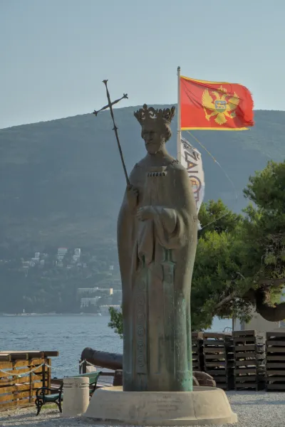 Portret spomenika kralju u Herceg Novom, Crna Gora, sa državnim grbom i morem u pozadini.