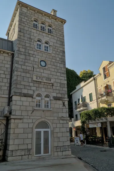 Kameni toranj sa satom u Herceg Novom, Crna Gora, sa plavim brojčanikom i ćiriličnim natpisom iznad luka.