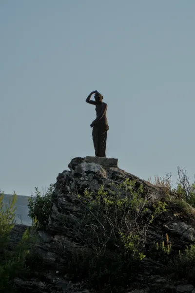 Bronzana statua žene na stenovitom izbočini na pozadini vedrog neba u Herceg Novom.