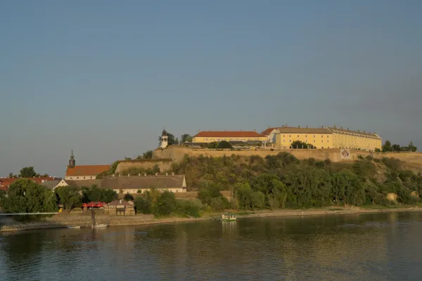 Петроварадинская крепость, Сербия, в теплом вечернем свете, с рекой и деревьями на переднем плане.