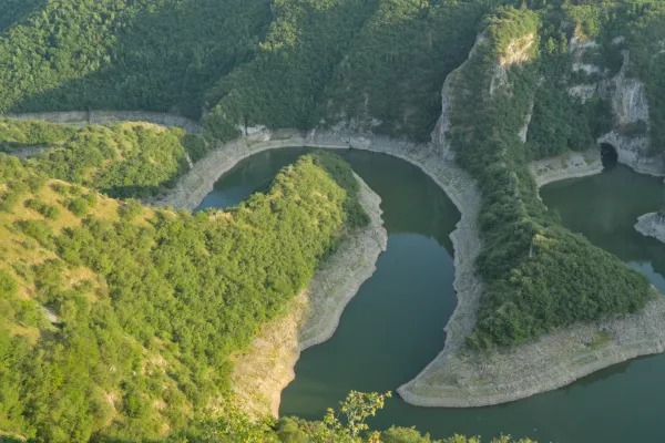 Windender Flusslauf unter der untergehenden Sonne, umgeben von grünen Hügeln in Serbien.