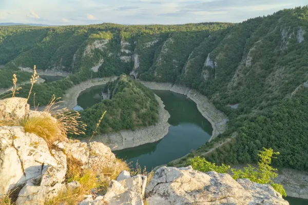 Flussbiegung des Uvac in Serbien bei Sonnenuntergang mit üppiger Vegetation und felsigen Ufern.