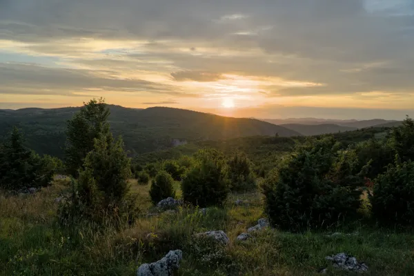 Sonnenuntergang über dem Uvac-Tal vom Aussichtspunkt Metlja, Serbien, mit dramatischen Wolken und sonnenbeschienenen Hügeln.