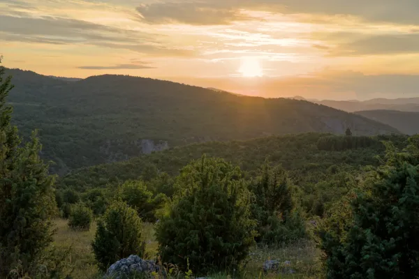 Panorama der Landschaft von Uvac, Serbien, mit sanften Hügeln und üppiger Vegetation, beleuchtet vom warmen Licht des Sonnenuntergangs.
