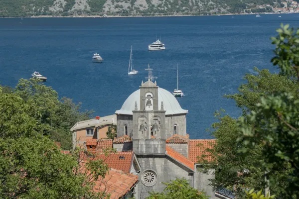 Iglesia abovedada con campanario al fondo de la Bahía de Kotor, Montenegro, cerca de Morinj, con yates en el agua.