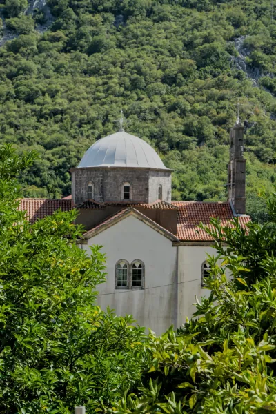 Church on the mountain in Morinj, Montenegro, surrounded by dense green foliage.