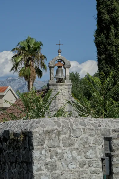Campanario de la Iglesia Católica de San Trifón en Kotor, Montenegro, con palmeras y montañas a lo lejos.