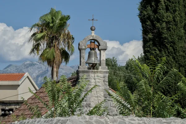 The "Bell Tower of St. Trivun's Church" in Kotor, Montenegro, under a clear blue sky with mountains in the background.