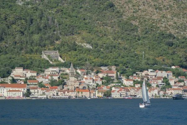 View of Perast in the Bay of Kotor with a sailboat and green hills in the background.