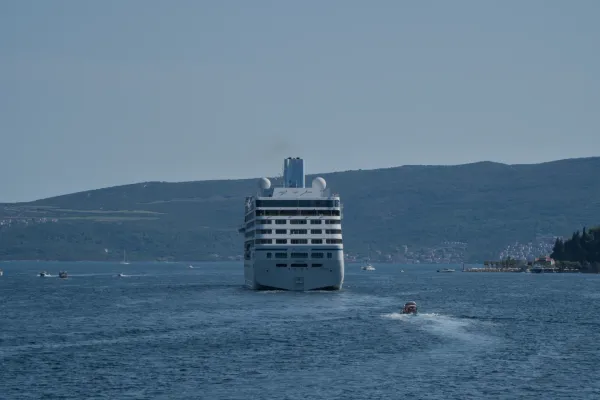 A cruise ship leaves Kotor Bay, surrounded by blue waters and green hills.