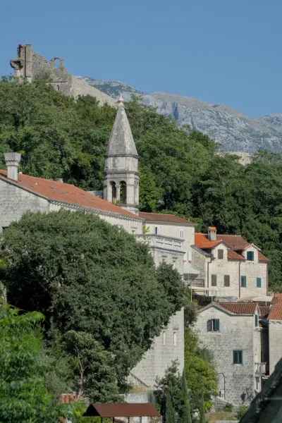 Fine art photograph from Perast, Montenegro, featuring stone buildings, a bell tower, and mountain backdrop.