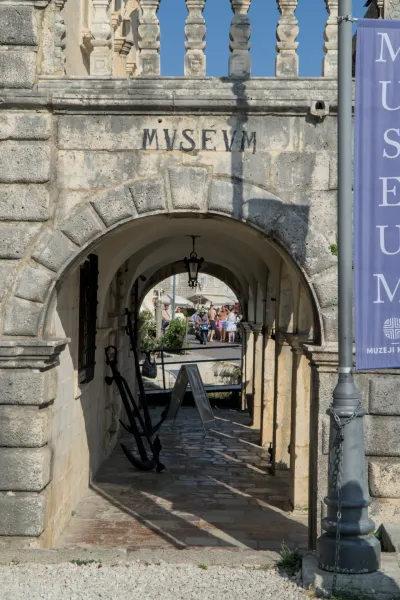 Ancient museum arch in Perast, Montenegro, adorned with historic anchors, overlooking a vibrant street.