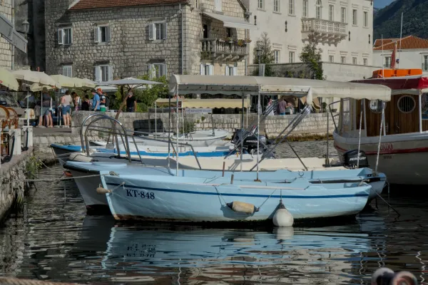 Imágenes de barcos en el puerto de Perast, Montenegro, con edificios de piedra al fondo.