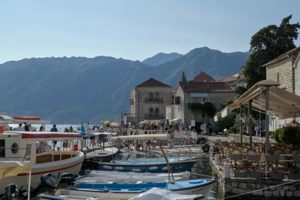 Sonniger Tag am Pier von Perast, Montenegro, mit Booten, historischen Gebäuden und Bergen im Hintergrund.