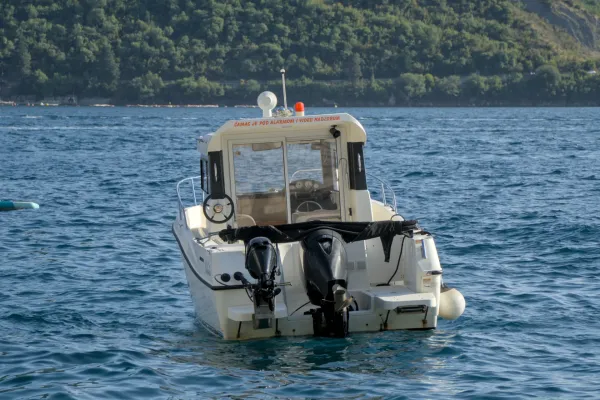 A boat waits for tourists in the calm waters of Perast, Montenegro, with green hills in the background.