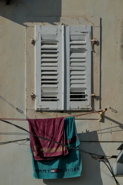Window with white wooden shutters in Perast, Montenegro, with colorful laundry hanging on a line.