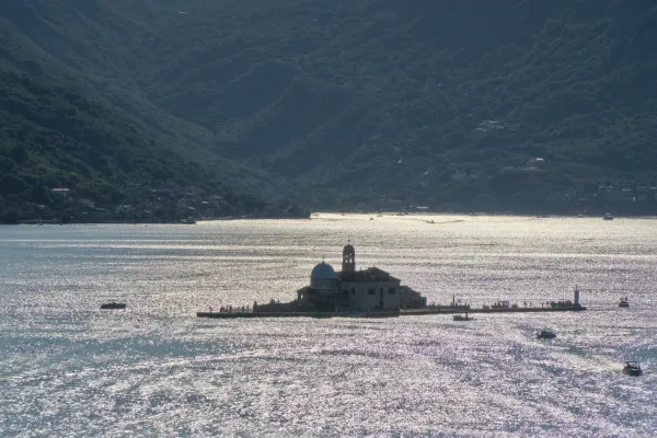 View of Gospa od Škrpelja island at sunset, with shadowy mountains in the background and shimmering water, captured from the tower in Perast.