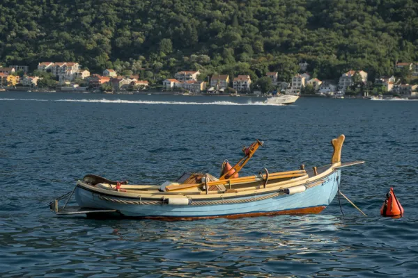 A light blue boat drifts on the calm waters of the Bay of Kotor near Perast, Montenegro.