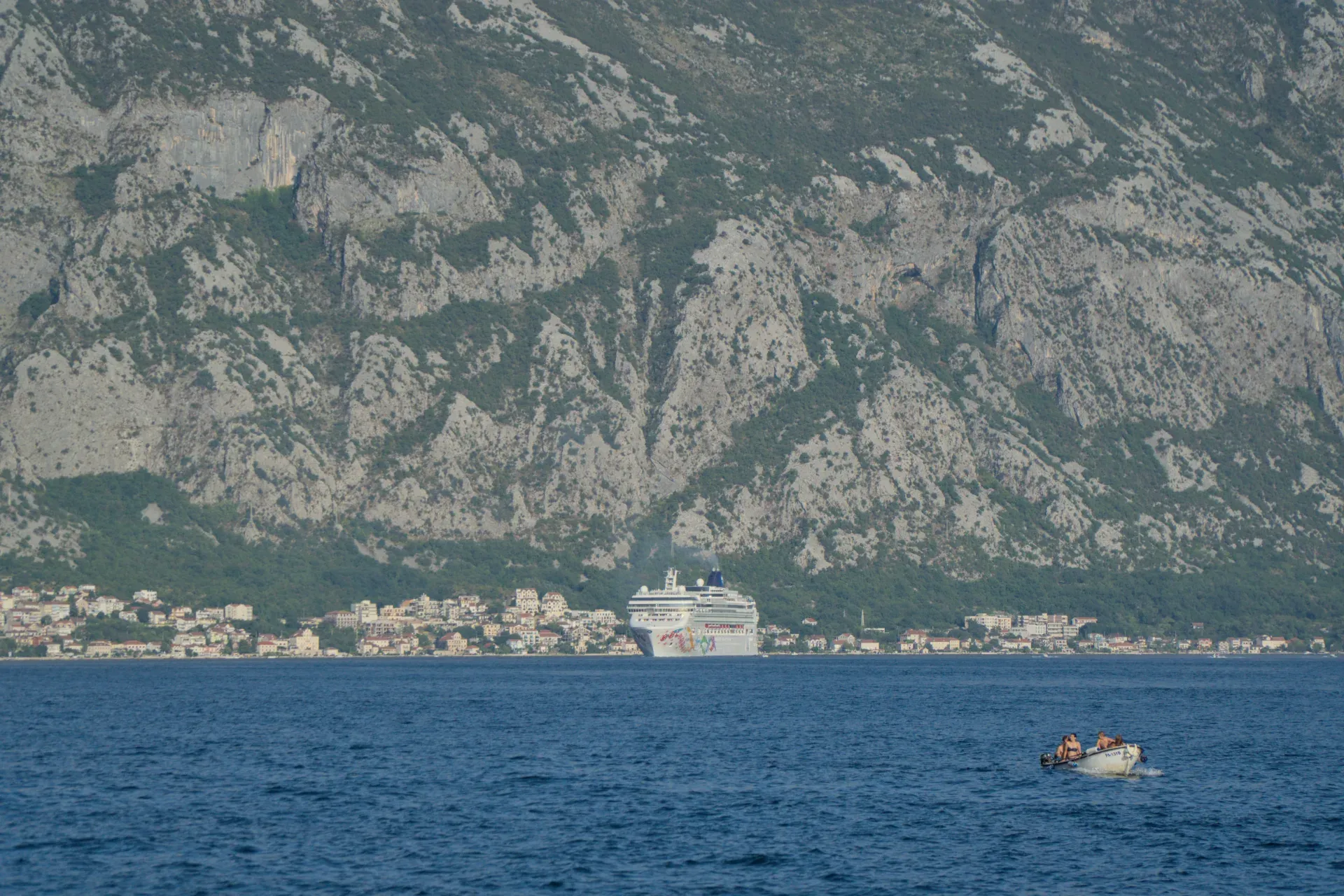 Crucero y pequeñas embarcaciones en el mar frente a Kotor con sus casas y montañas detrás.