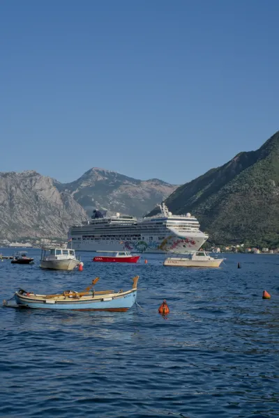 Gran crucero saliendo de la bahía de Kotor a través de Perast, con pequeños barcos en primer plano.
