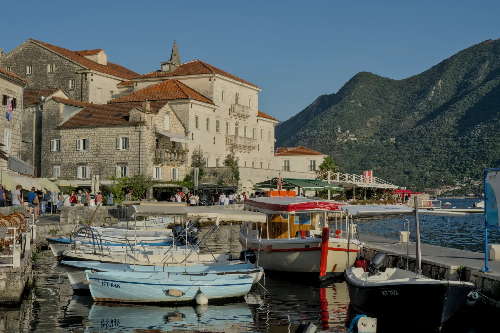Perast, Montenegro, capturado en la hora dorada, con barcos en el puerto y montañas al fondo.