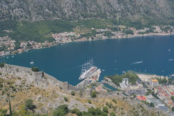 Large sailboat moored at the pier in the Bay of Kotor, Montenegro, with ancient fortifications in the foreground.
