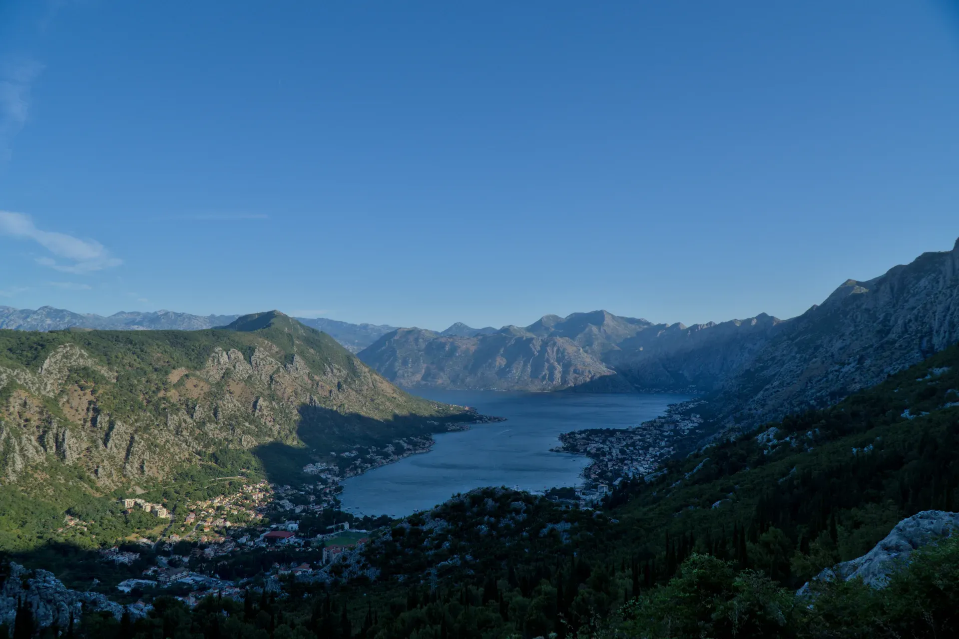 Vista previa del amanecer de la bahía de Kotor, Montenegro, con vistas a la ciudad y las montañas desde una carretera de montaña serpenteante.