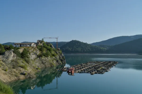 Morgendämmerung am Zaovine-See, Serbien. Ruhiges Wasser spiegelt Berge und klaren Himmel mit schwimmenden Strukturen wider.