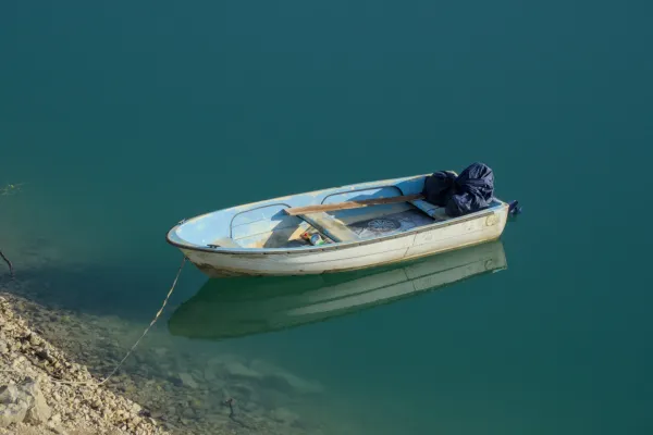 Beli čamac sa plavim detaljima, privezan, plovi mirnom tirkiznom vodom Zaovinskog jezera u zoru.