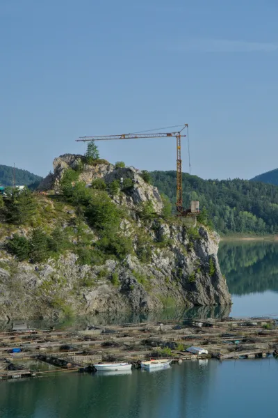Morning view of Zaovine Lake featuring a crane on a cliff and floating fish farms in the foreground.