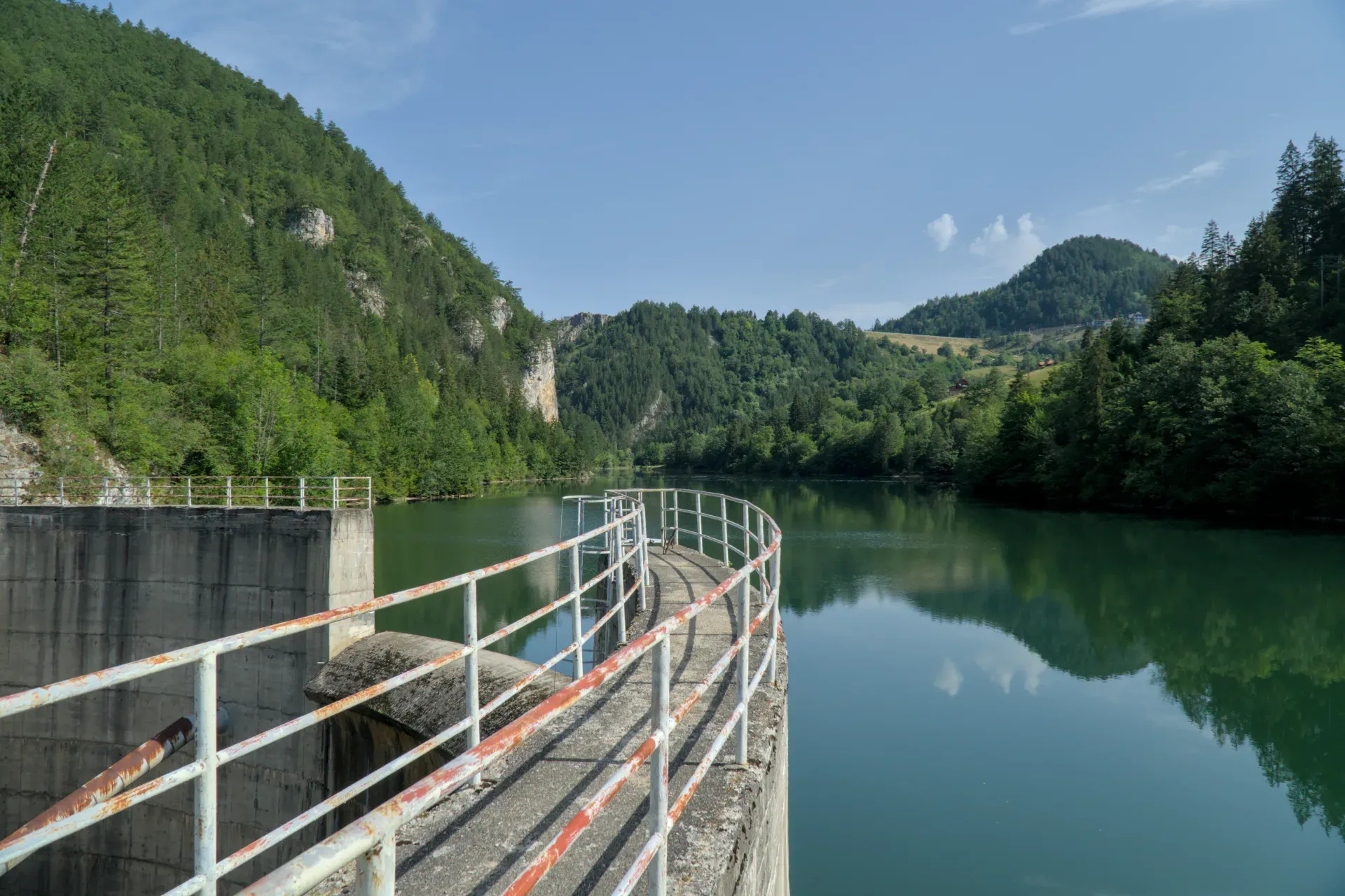 Presa del lago Spajići en Serbia con una pasarela curva y un exuberante paisaje montañoso verde.