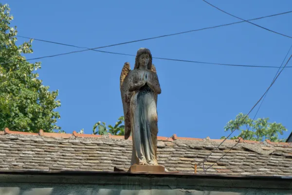 Engelsstatue auf einem Hausdach in Novi Sad, Serbien, vor blauem Himmel.