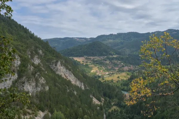 Vue panoramique depuis Ravna Stena surplombant le village de Spaichi dans le parc national de Tara, Serbie, avec des collines boisées et une rivière.
