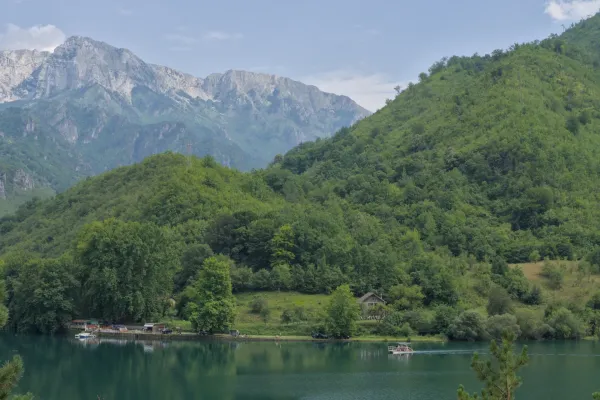 Paysage pittoresque sur la route de Sarajevo à Mostar : lac de montagne avec un bateau et des collines vertes sous un ciel nuageux.