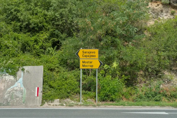 Wegweiser Richtung Mostar und Sarajevo inmitten von üppigem Grün, der eine wichtige Route markiert.